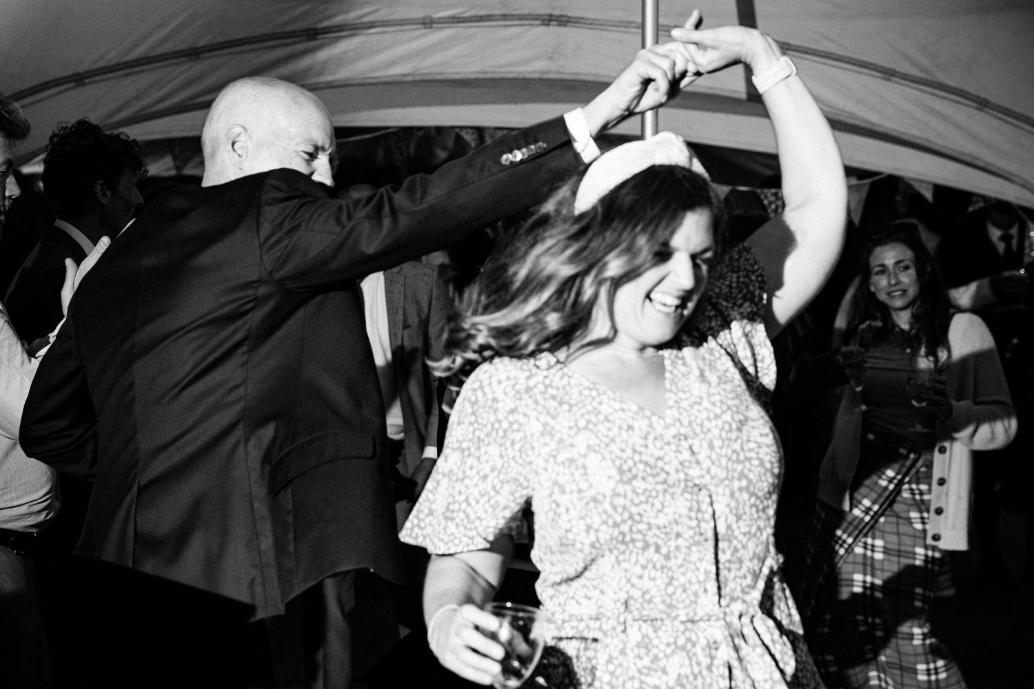 Wedding reception dance floor filled with celebrating guests under tent lighting.