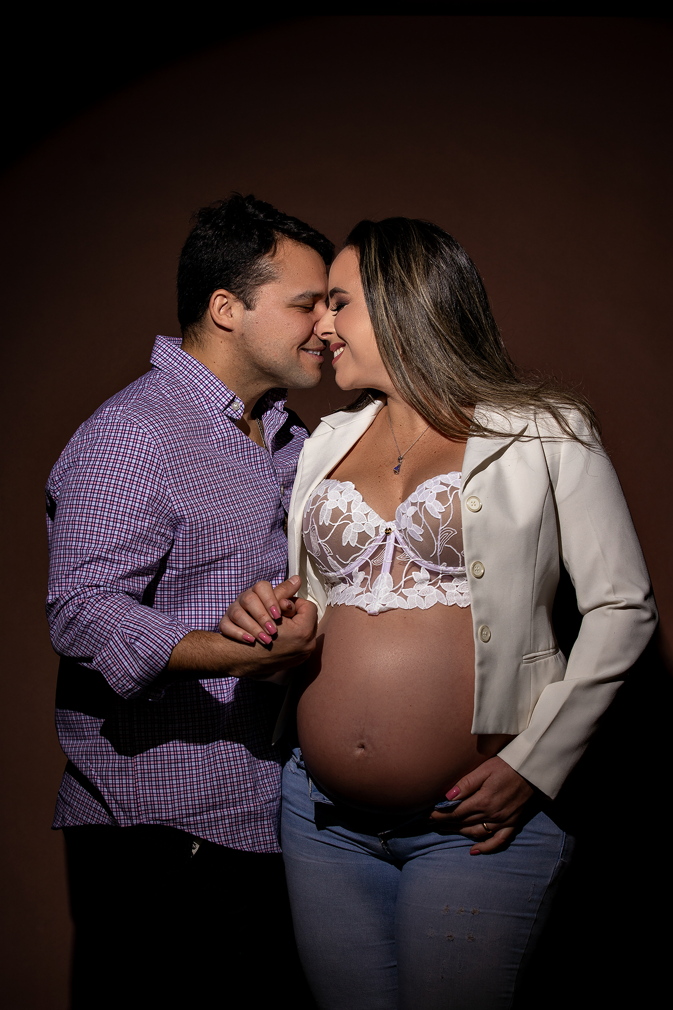 Romantic maternity studio photo with couple sharing intimate moment against dark backdrop.