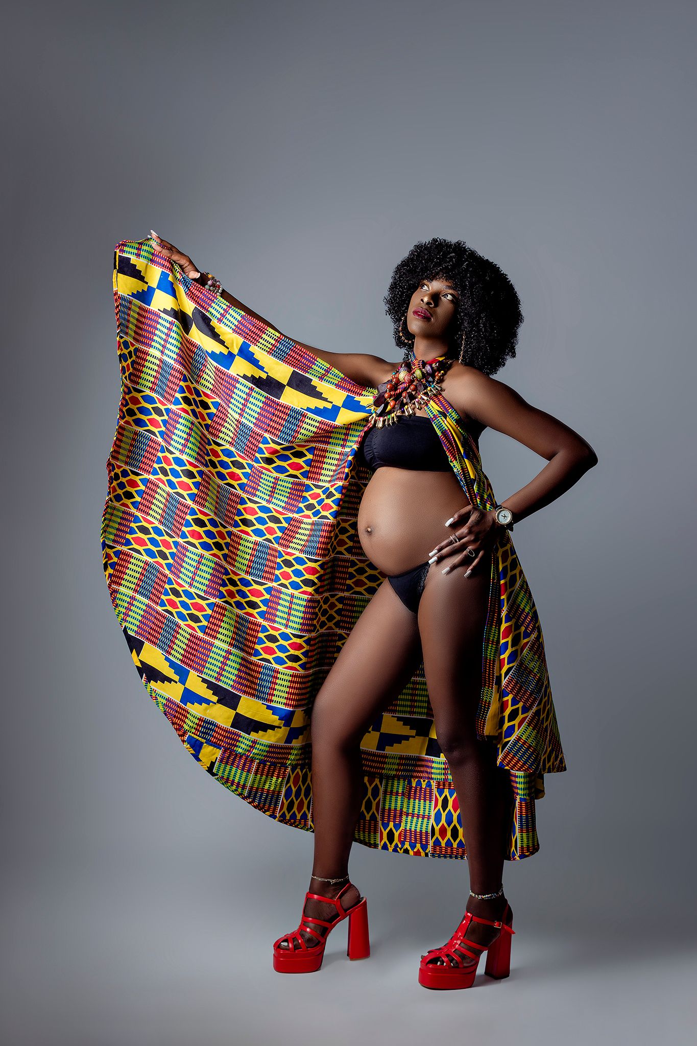 Artistic portrait with colorful African print fabric and red heels against grey background.
