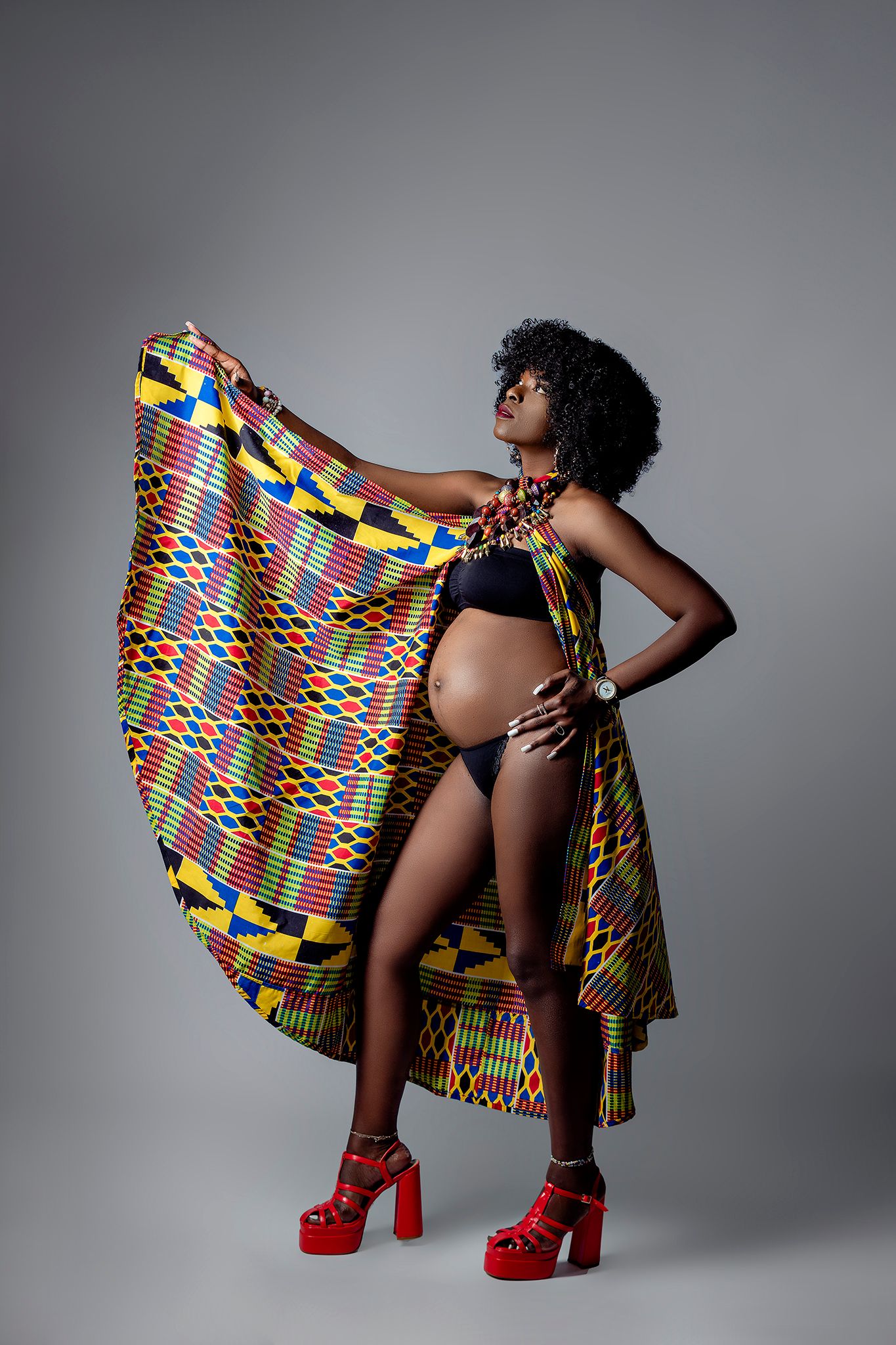 Fashion photo featuring vibrant kente cloth and red platform shoes on grey backdrop.