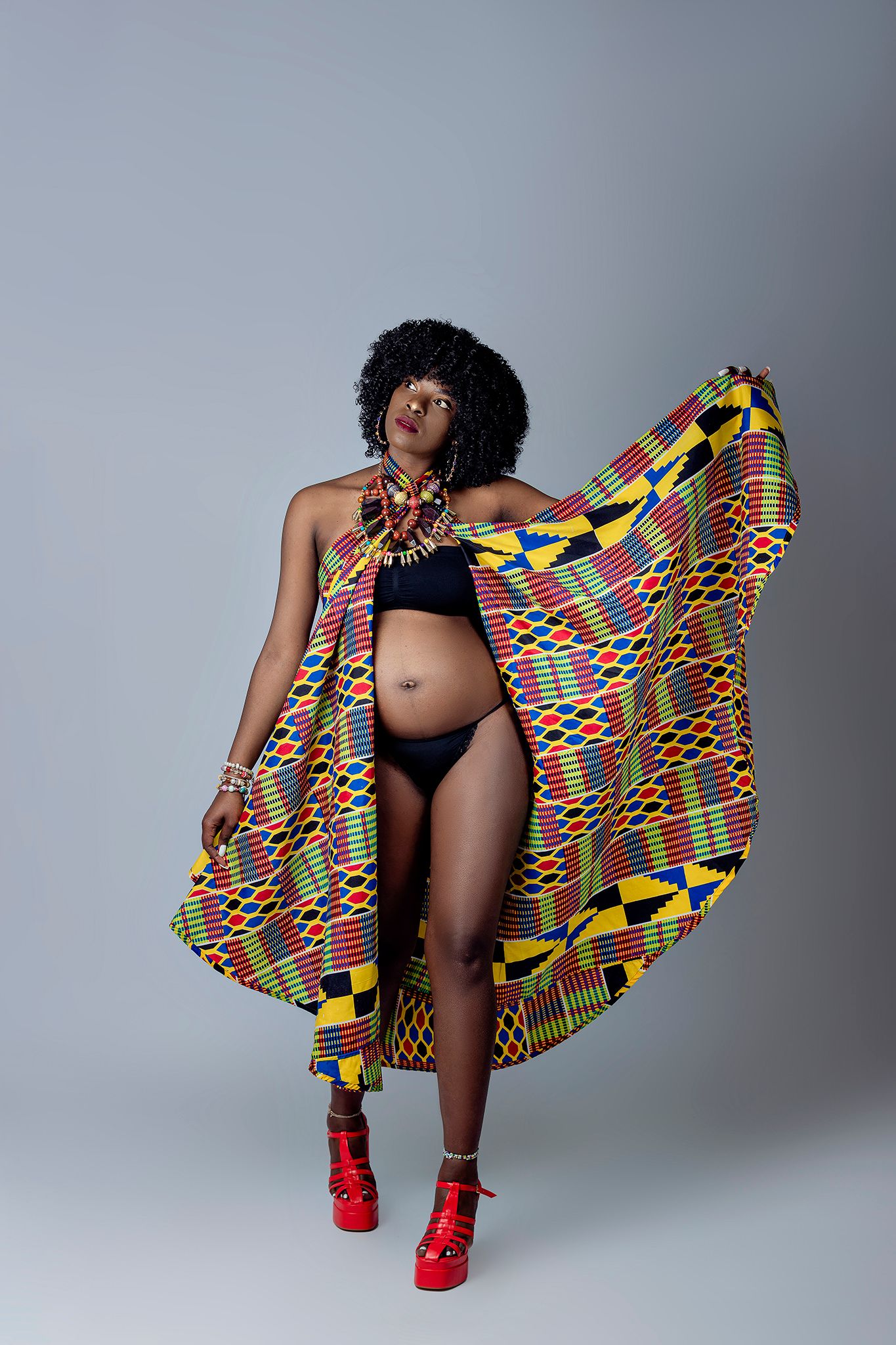 Maternity photo with traditional African print fabric and red heels in studio setting.