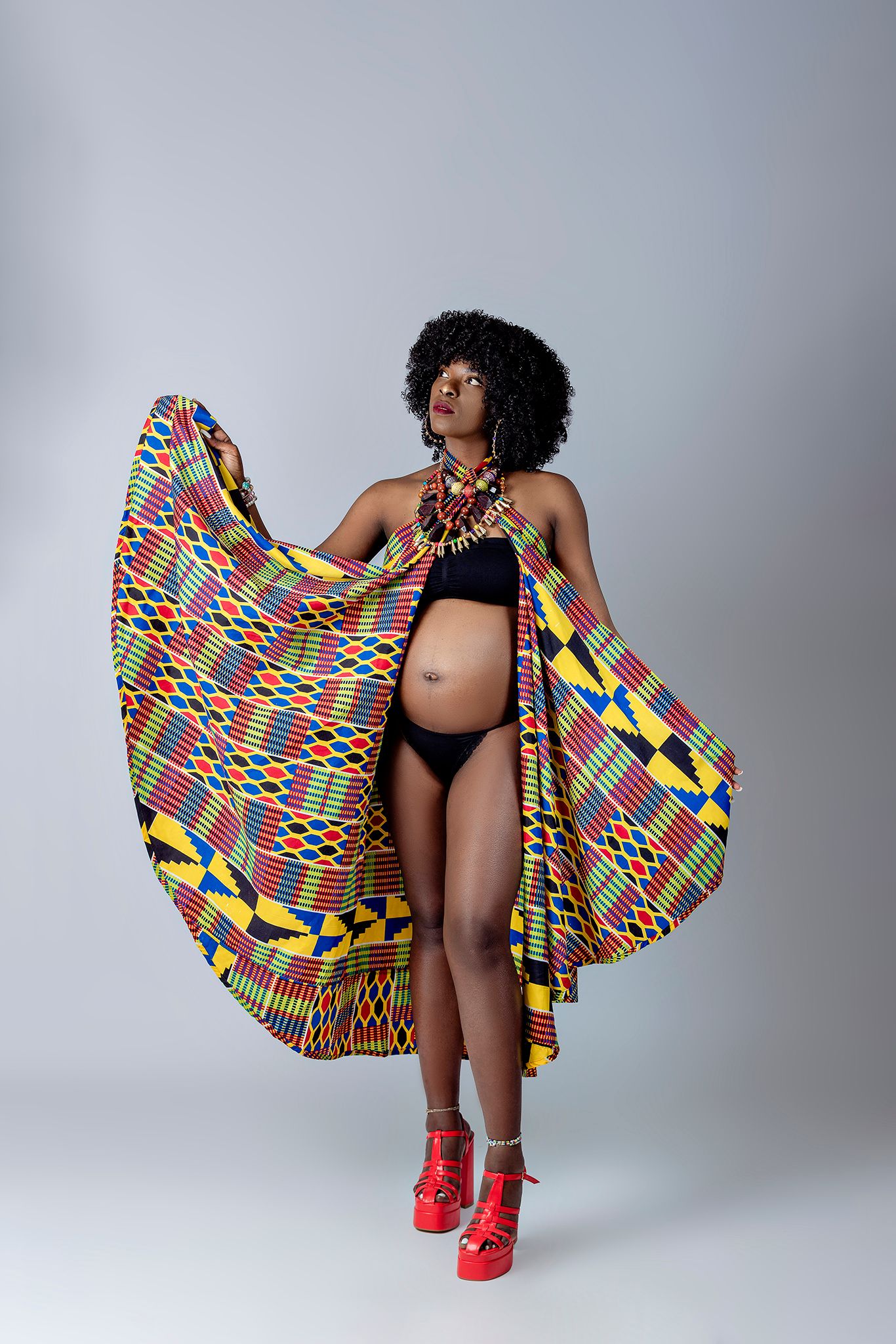 Creative maternity portrait with bold patterned fabric against neutral background.