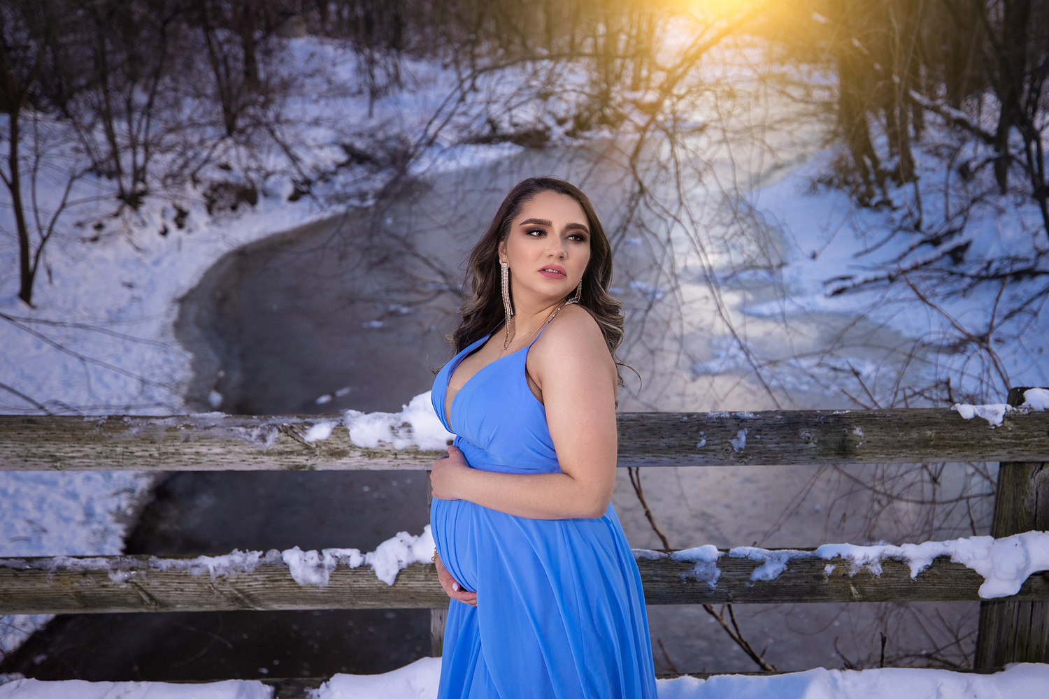 Elegant maternity photo on snowy steps with woman in vibrant blue dress.