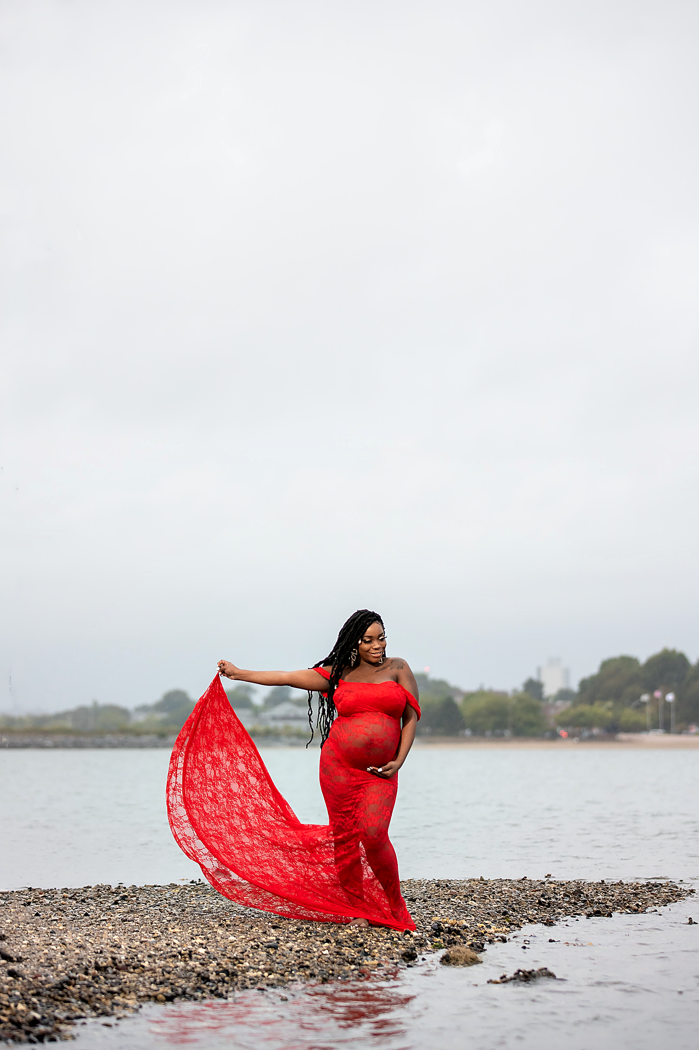 Maternity photo of woman in flowing red dress by waterfront.