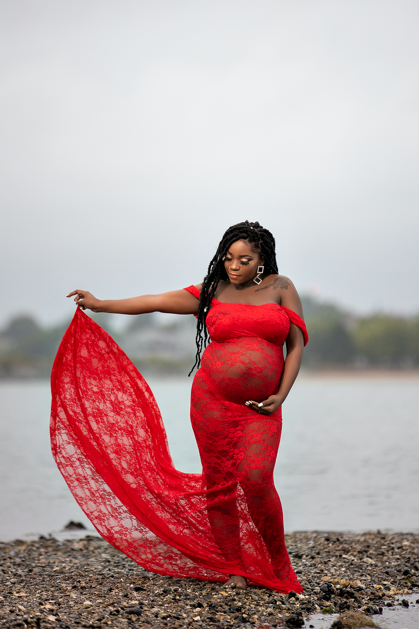 A flowing red lace dress billows dramatically against a misty waterfront backdrop.