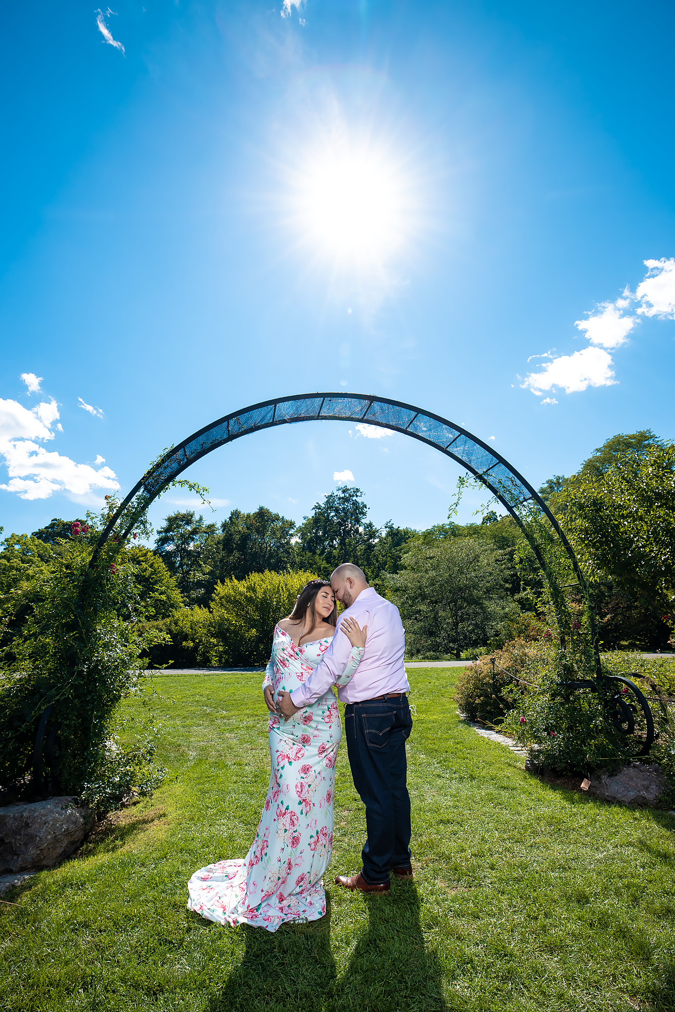 Couple embracing under garden archway on sunny day with blue sky.