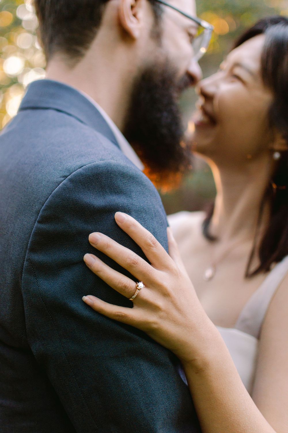 Close-up of a bride's engagement ring on groom's shoulder as the couple shares a joyful intimate moment.