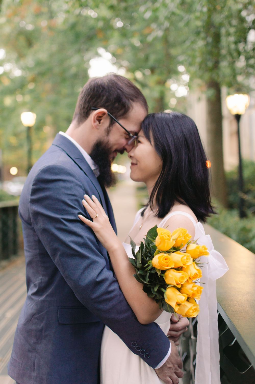 An engaged couple shares an intimate nose-to-nose moment on a bridge, bride holding yellow tulip bouquet.