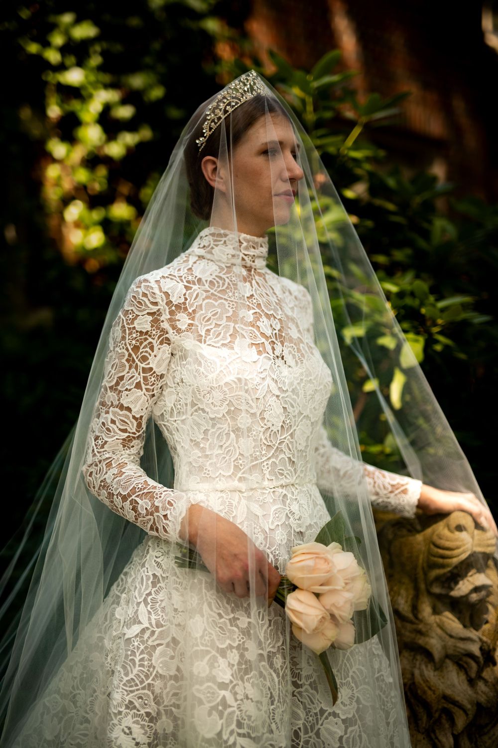 Delicate lace wedding dress with high neckline and long sleeves photographed in dappled sunlight.