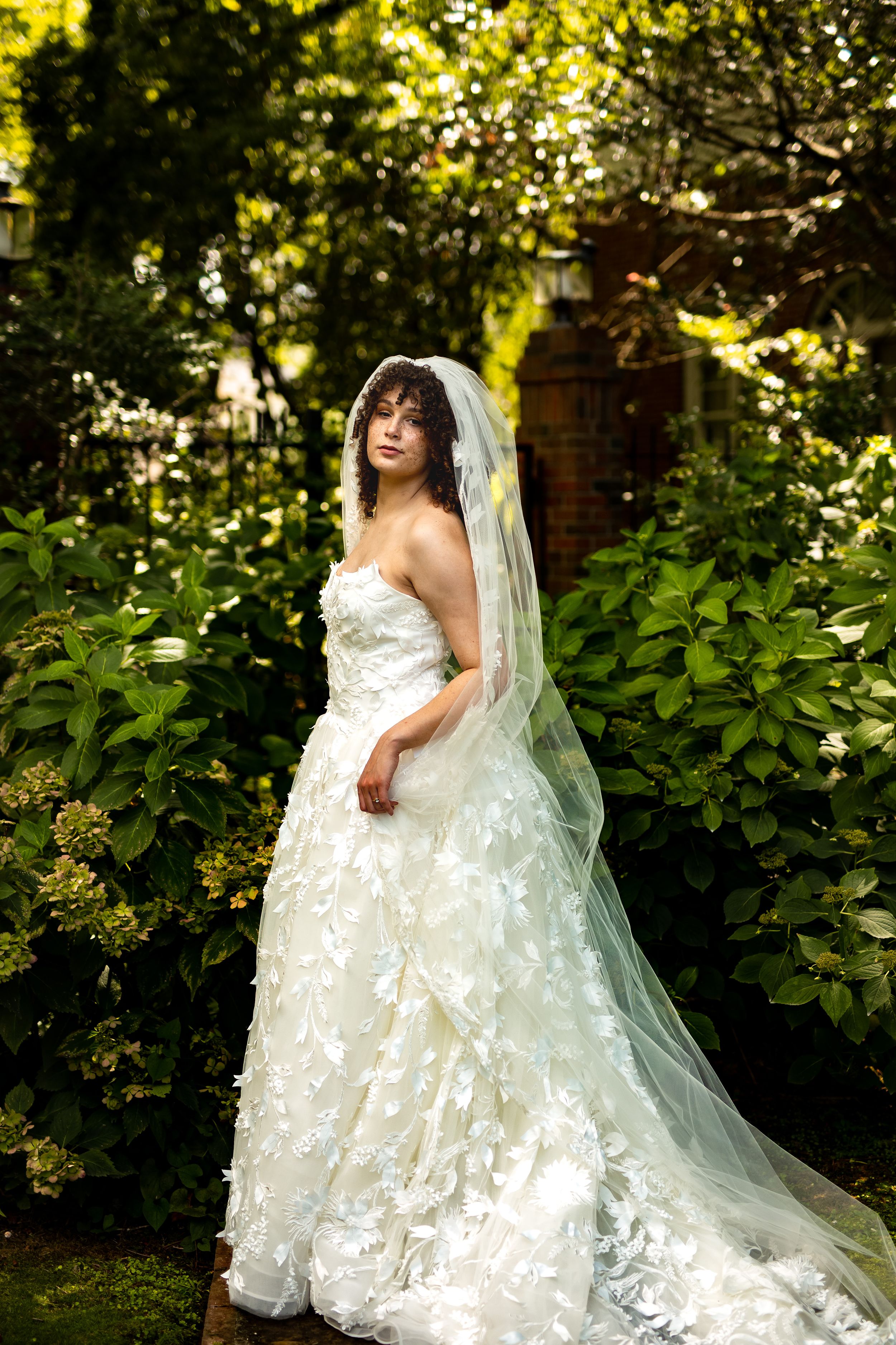 A stunning bridal portrait showcasing an elegant lace wedding gown and veil in a sunlit garden setting.