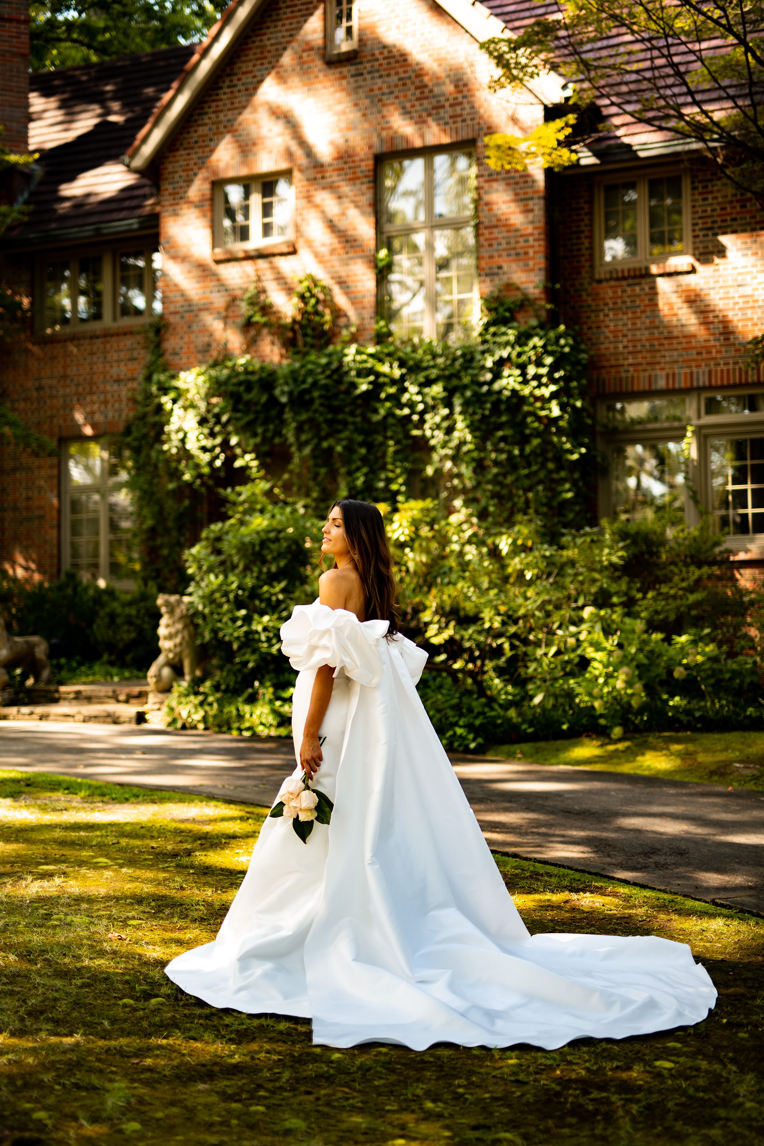 Wedding dress train spread beautifully on grass with brick building in background.