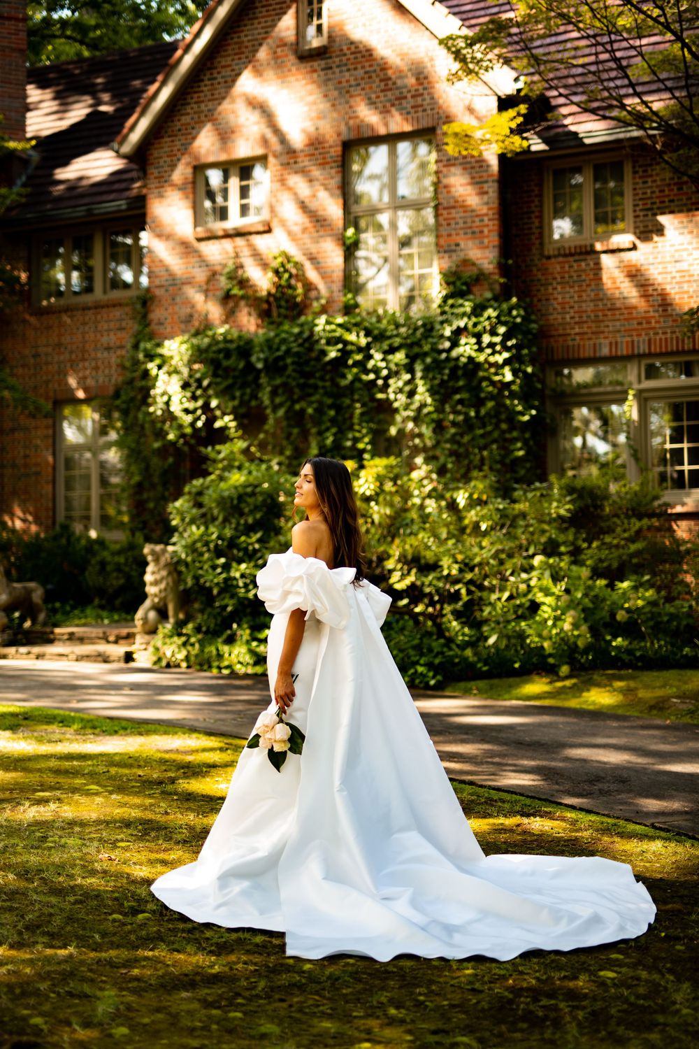 Wedding dress train spread beautifully on grass with brick building in background.