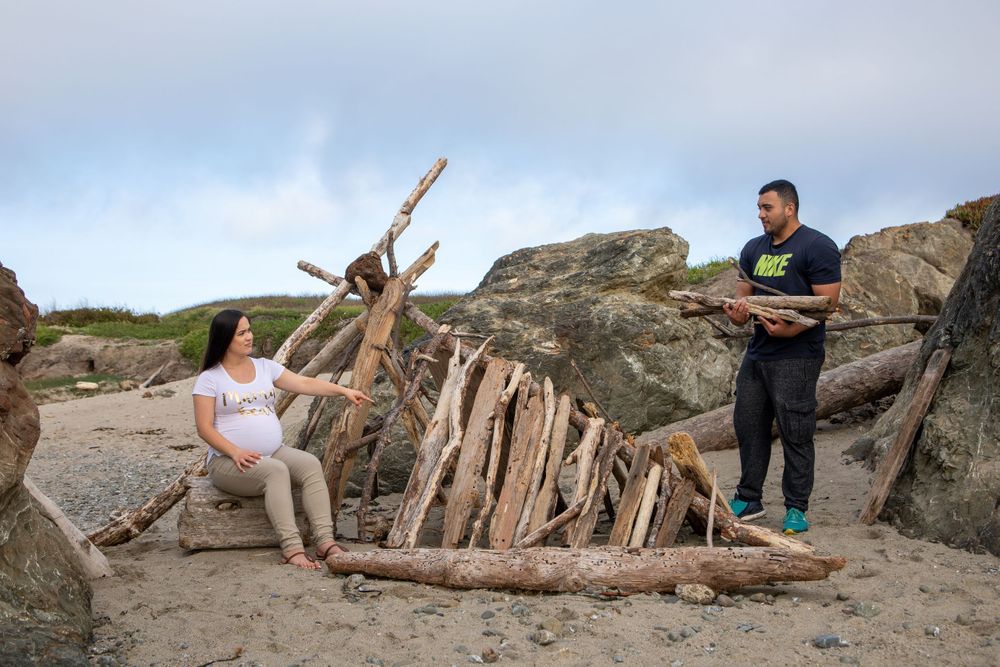 A beachside scene with driftwood structures against rocky coastal formations at sunset.