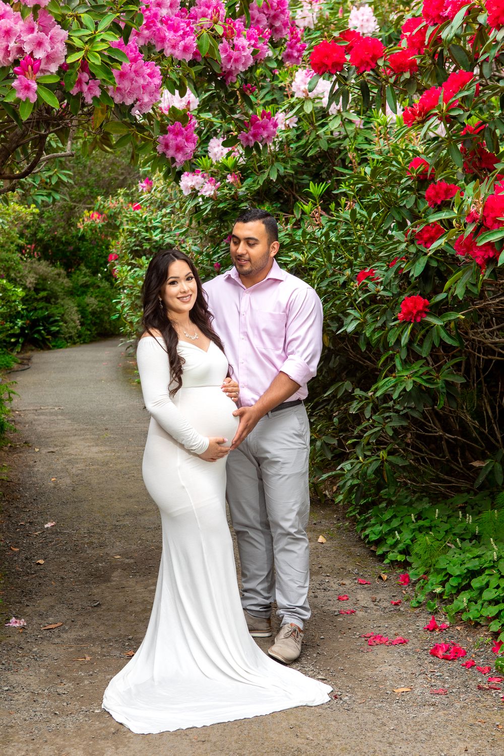 A maternity photo with a white dress against blooming red and pink rhododendrons.