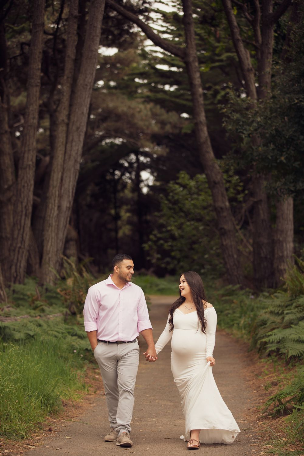 A romantic walk along a tree-lined path in long white dress and pink shirt.