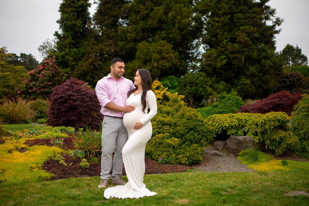 A romantic maternity photoshoot in a lush garden with colorful flowers and shrubs.