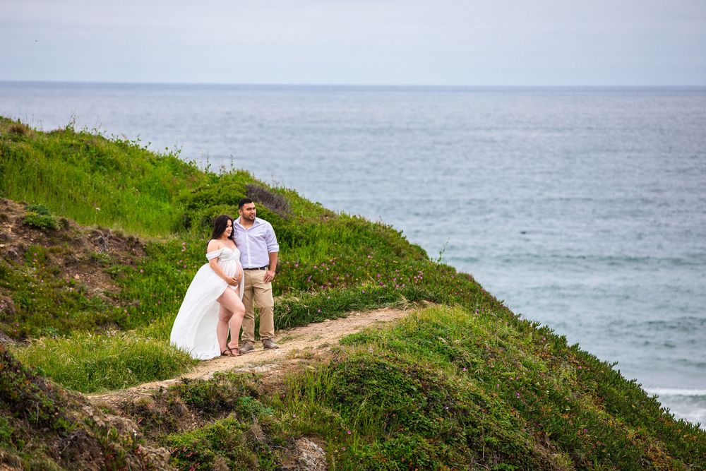 A couple shares a romantic moment on a clifftop path overlooking the ocean.