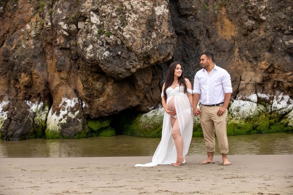 A romantic beach photoshoot near dramatic rocky cliffs and ocean waves.
