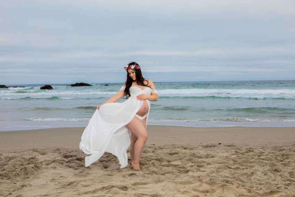 A flowing white dress billows in the ocean breeze during a beach photoshoot.