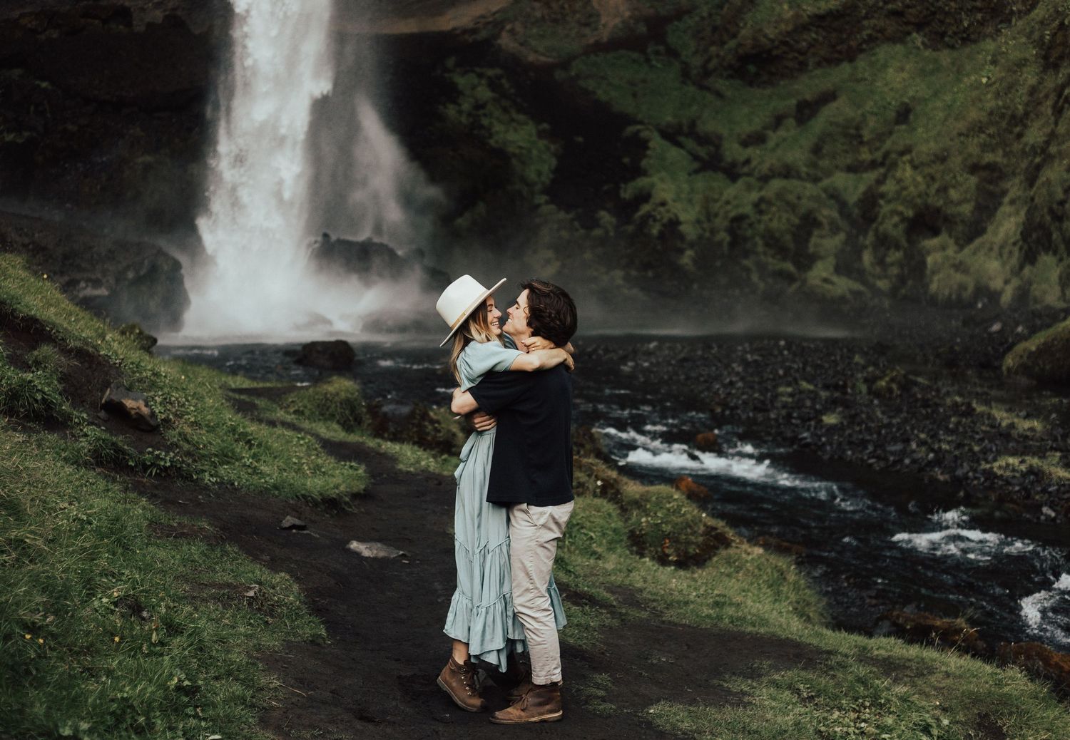 engaged couple embracing in green landscape of iceland waterfall