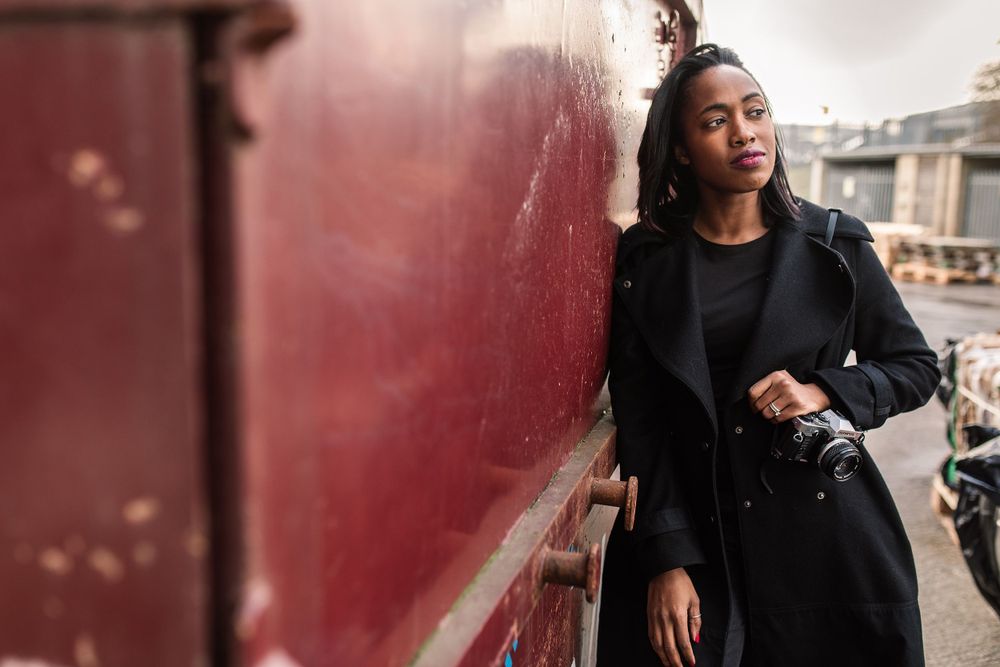 Brand Photographer in Hertfordshire Becky Harley Creative Oleesha leaning against red wall holding camera on brand shoot