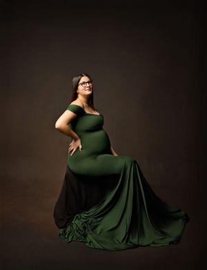 New Hampshire maternity photography featuring a pregnant woman in a deep green gown, elegant studio portrait with dramatic lighting