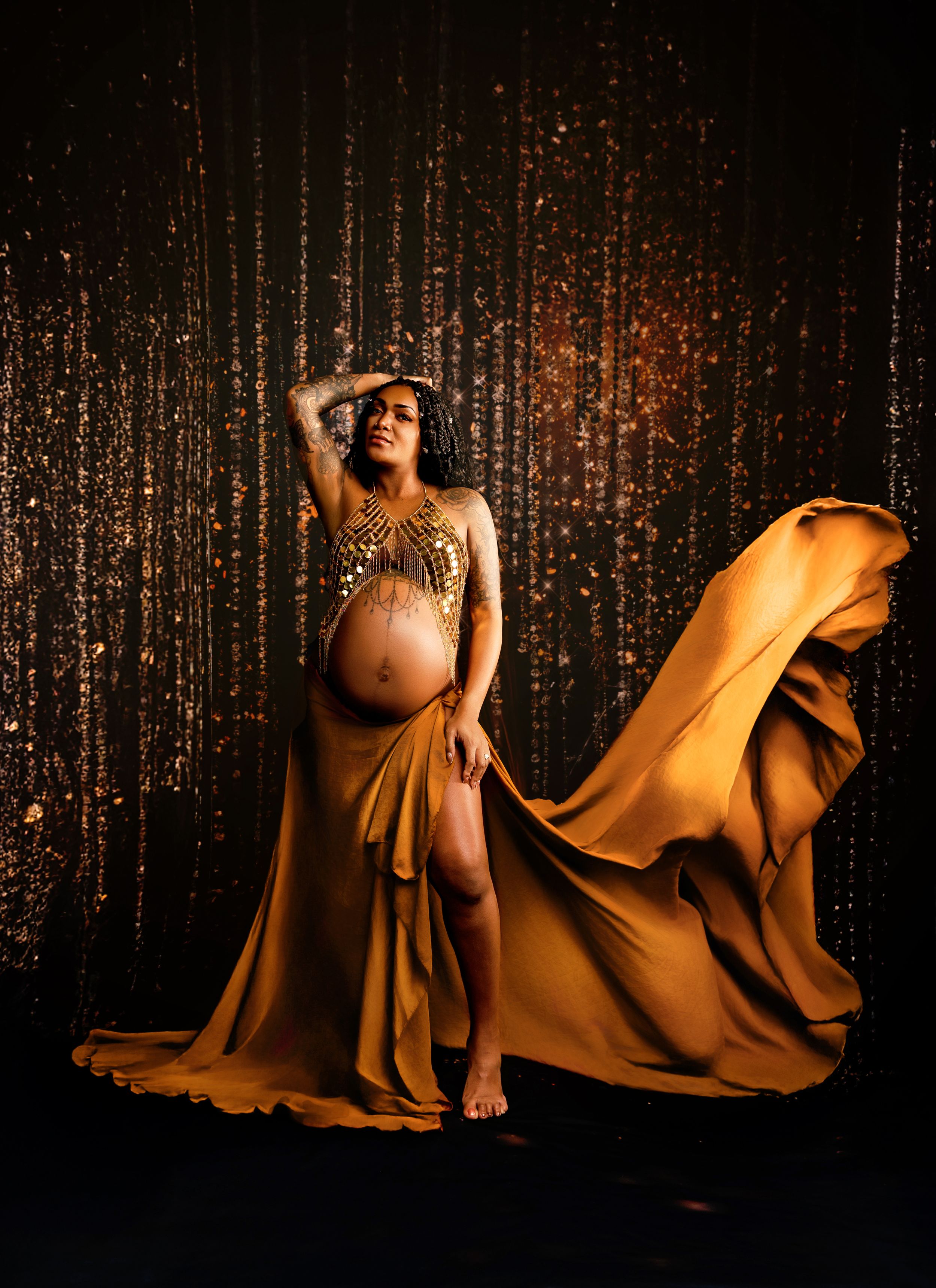 Elegant maternity portrait in Tilton NH featuring a flowing gold gown and artistic studio backdrop in the Lakes Region.