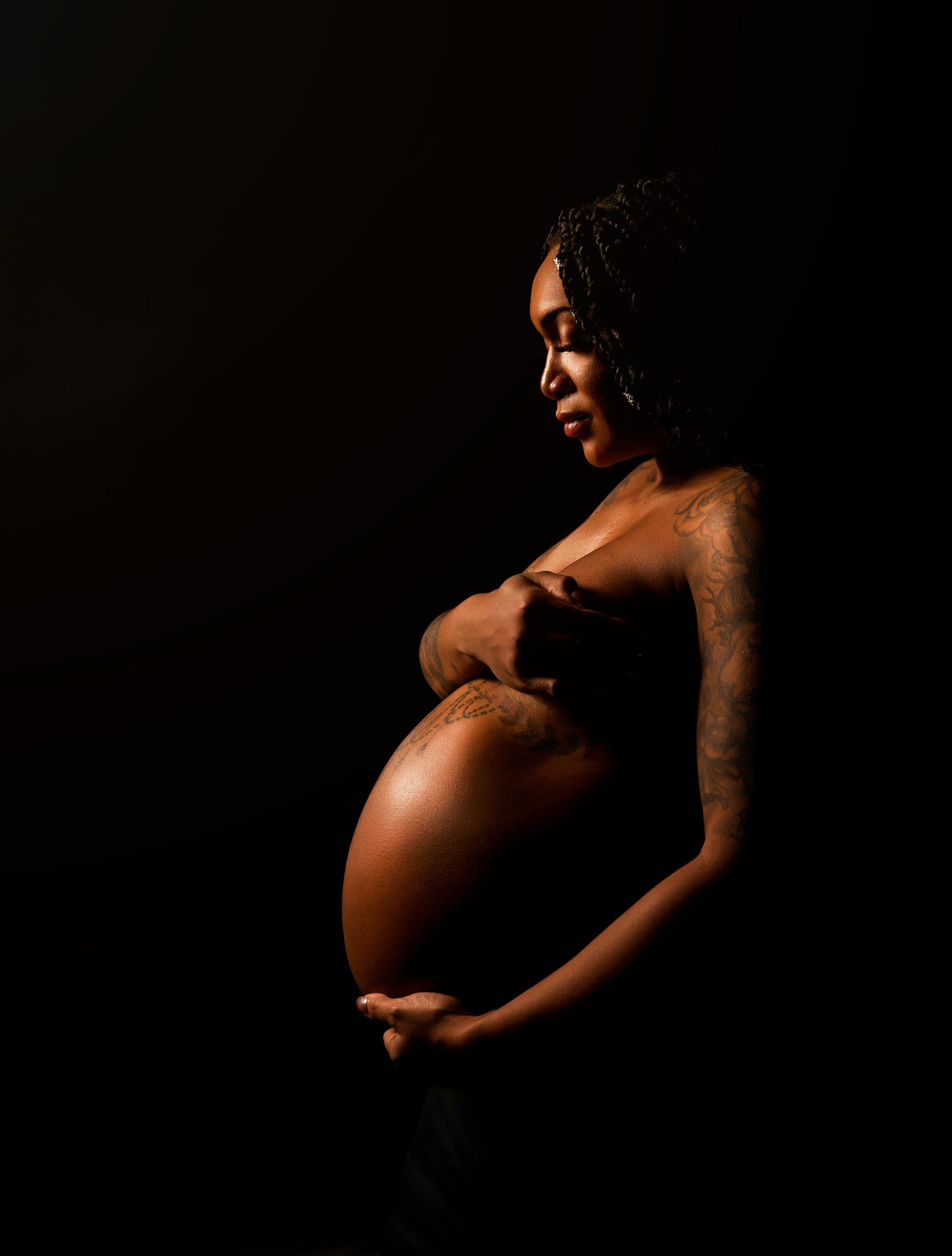 Side profile maternity portrait of a pregnant woman in a Tilton NH studio, highlighting her baby bump with soft dramatic light.
