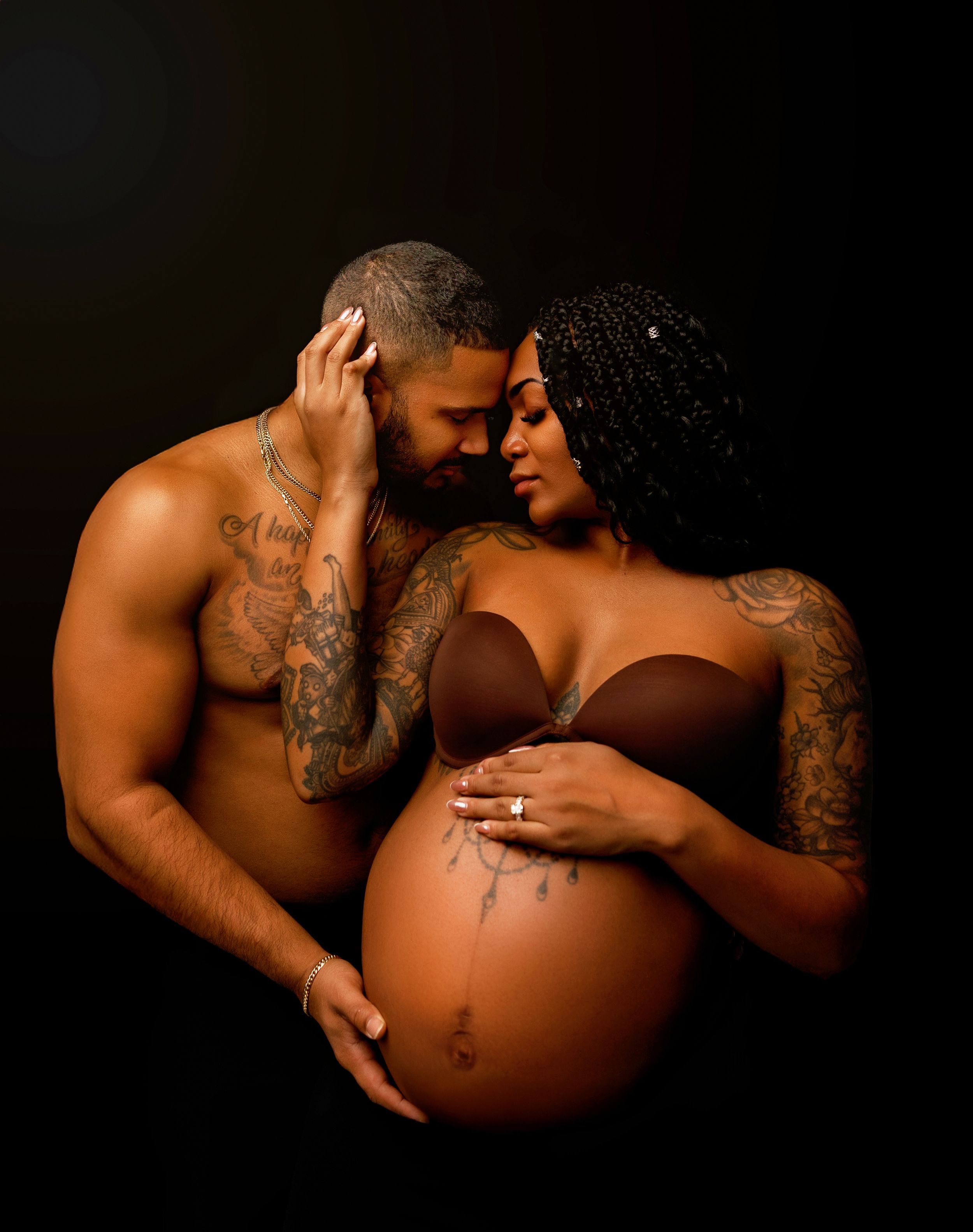 Intimate studio maternity portrait of an expecting couple in Tilton NH, photographed with dramatic lighting in a dark studio.