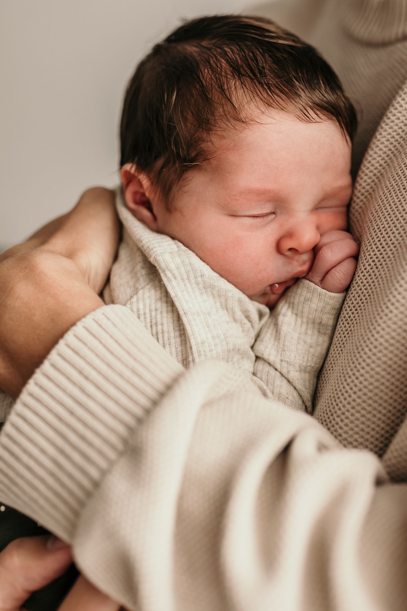 Close-up of sleeping newborn nestled in cozy cream-colored knit fabric.