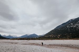 Einsame Figur steht auf dem felsigen Flussbett vor dem Hintergrund einer nebligen Berglandschaft. Reute