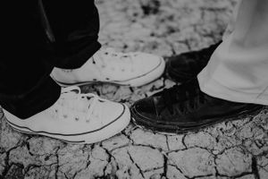 Schwarz-weiße Nahaufnahme von kontrastierenden weiß-schwarzen Turnschuhen auf rissigem Boden. Forgensee