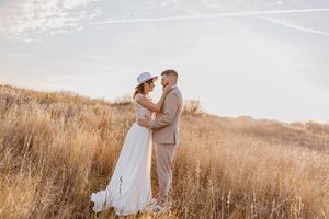 Ein romantisches Hochzeitsporträt eines Paares, das sich in einem sonnenverwundeten Feld aus goldenem Gras umarmt.