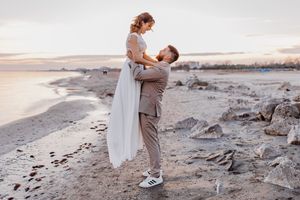 Romantische Strandhochzeitsszene mit Paar, das sich am felsigen Ufer bei Sonnenuntergang umarmt.
