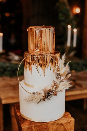 Moderne dreistufige Hochzeitstorte mit goldenem Tropfeffekt und getrockneten Blumenakzenten.
