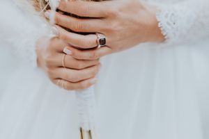 Nahaufnahme von Händen, die getrocknete Blumen halten und Verlobungsring und Ehering zeigen.