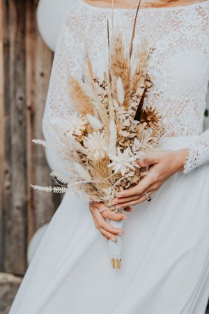 Neutraler getrockneter Blumenhochzeitsstrauß mit Pampasgras gegen weißes Spitzenkleid.