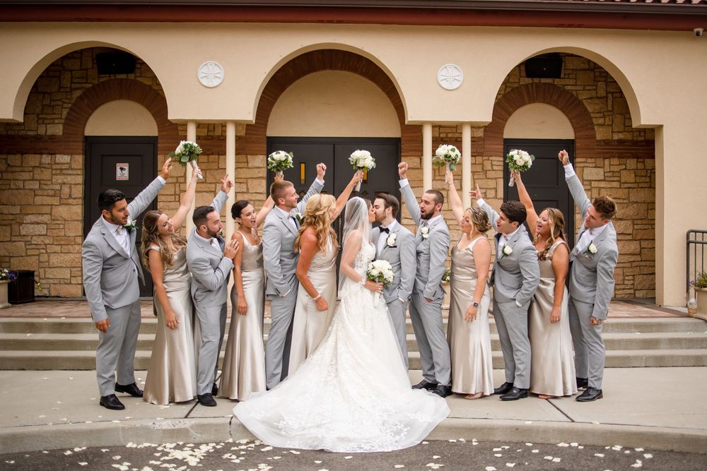 Wedding party in gray attire celebrating on stone steps with confetti.