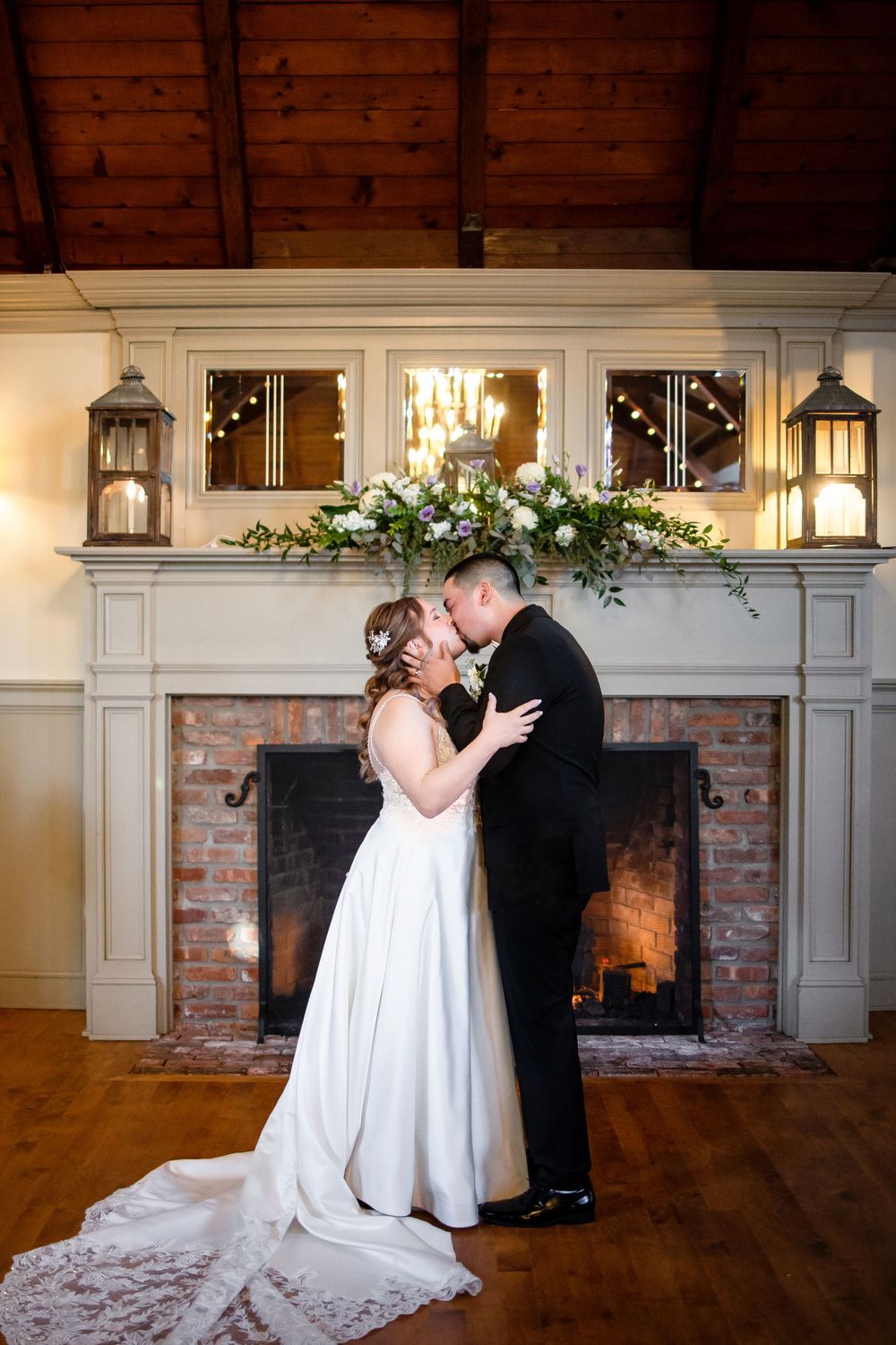 Romantic wedding moment in front of a beautifully decorated fireplace with white floral arrangements.