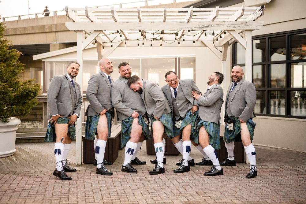 Wedding party wearing traditional Scottish kilts and gray suit jackets pose together outdoors.