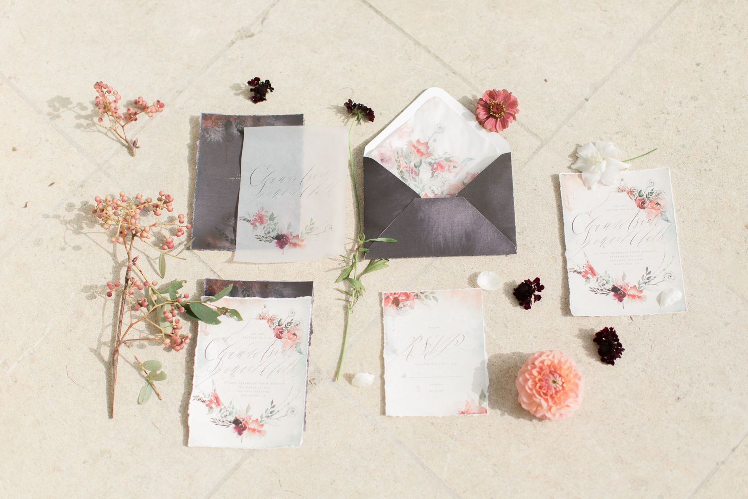 Elegant wedding stationery with coral pink flowers and black envelopes arranged on a light beige surface euridge manor