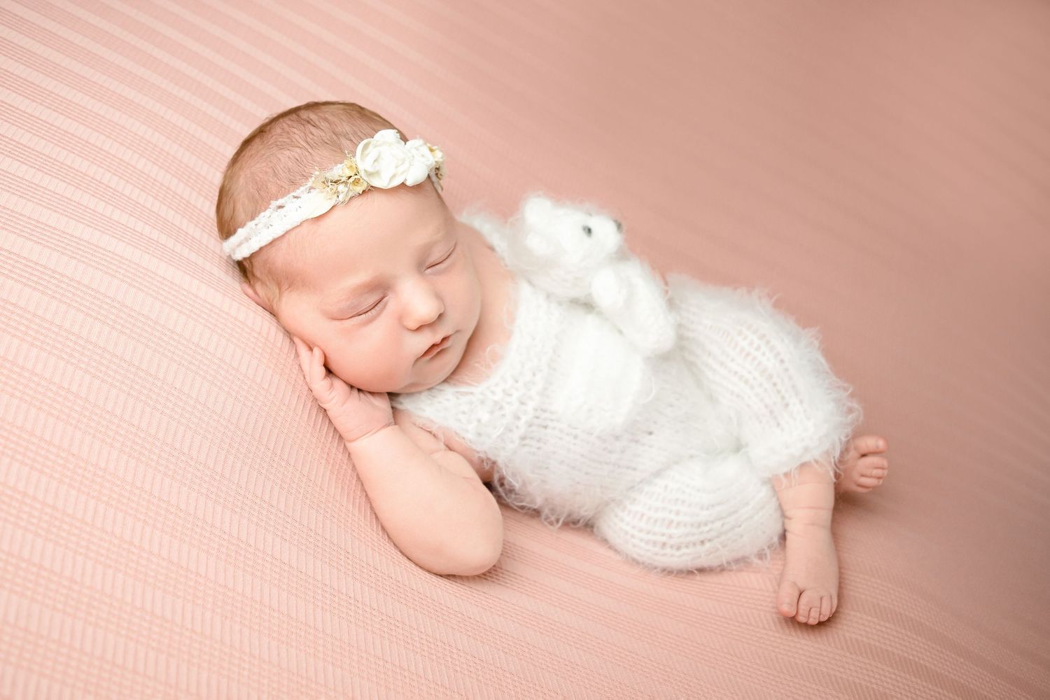 Newborn baby girl in white fluffy romper sleeping on pink striped backdrop taken by heather katie photography