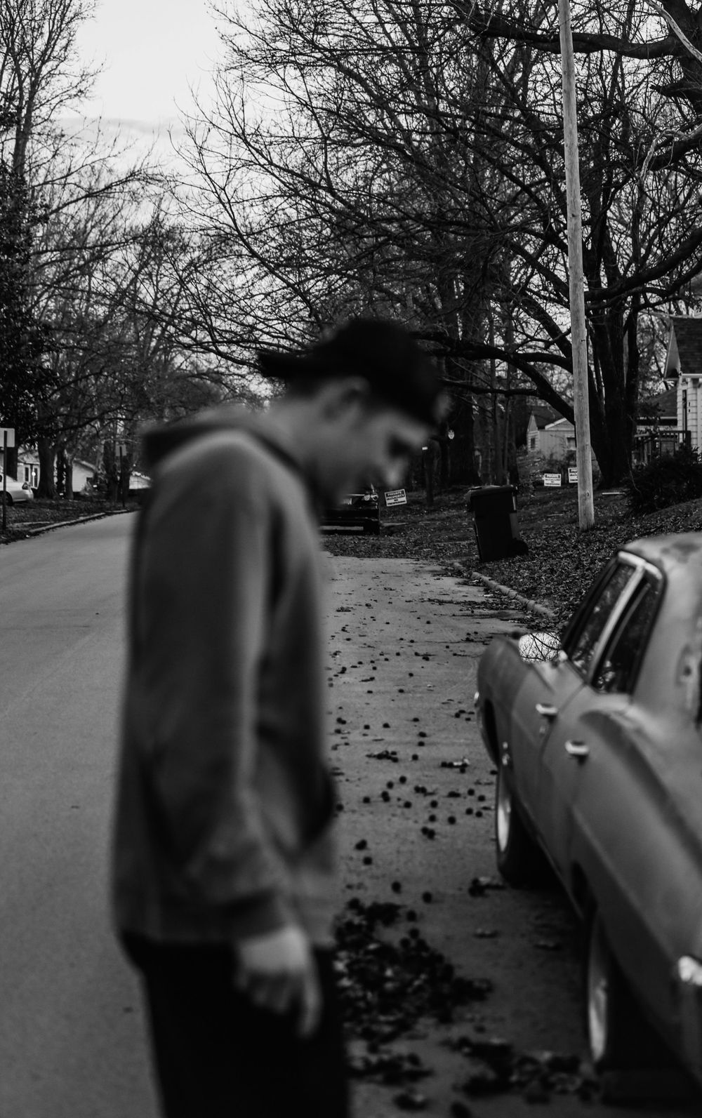 black and white photo of guy holding long board by old car