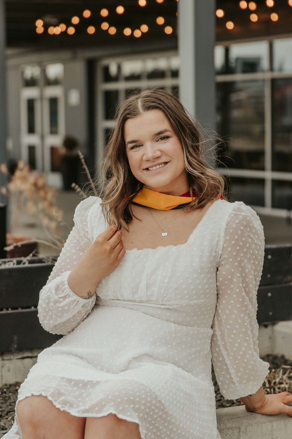 girl in white dress for college graduation with twinkly lights in the background