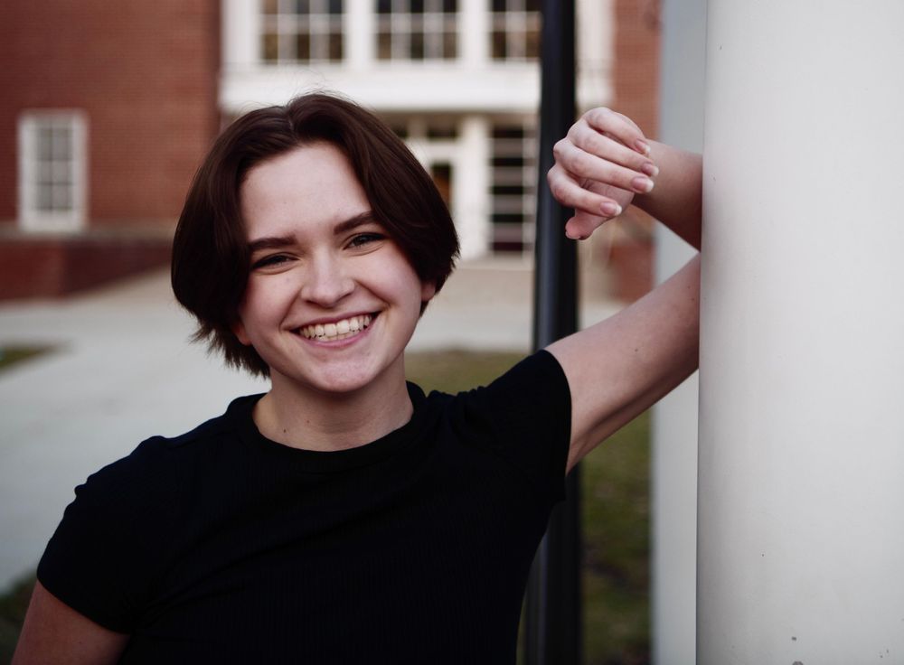 Johnie leaning against a pole and smiling at the camera