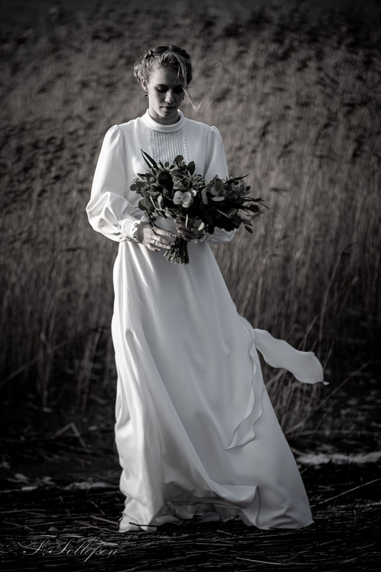 Elegant bride in a flowing white gown holding a bouquet in a dramatic black and white portrait.