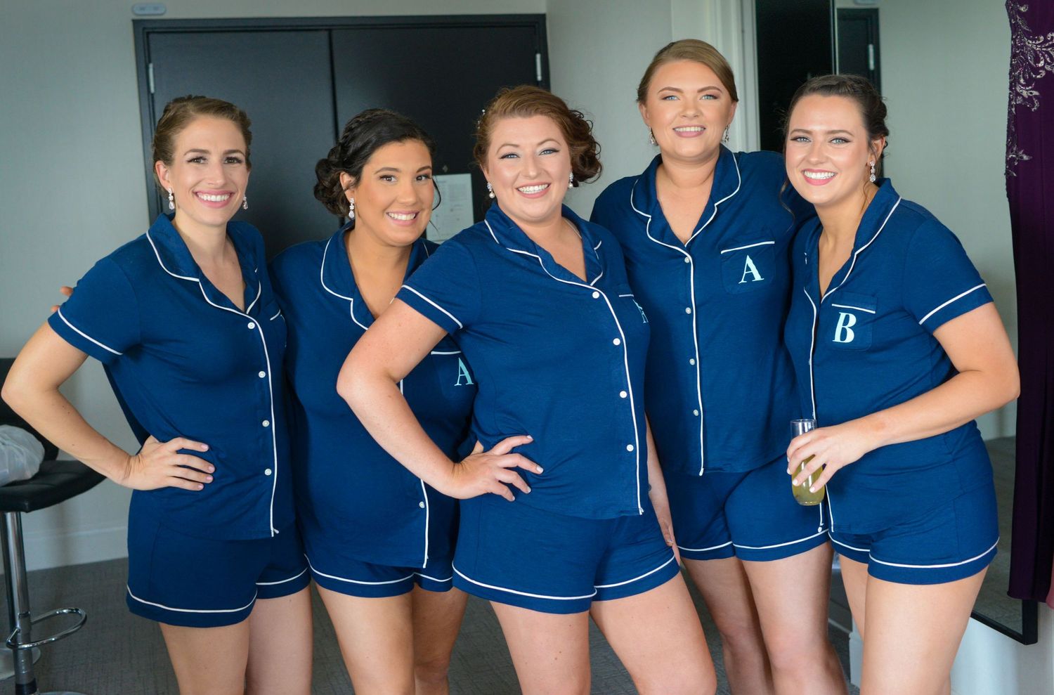 Five women pose together wearing matching navy blue and white piped pajama sets.