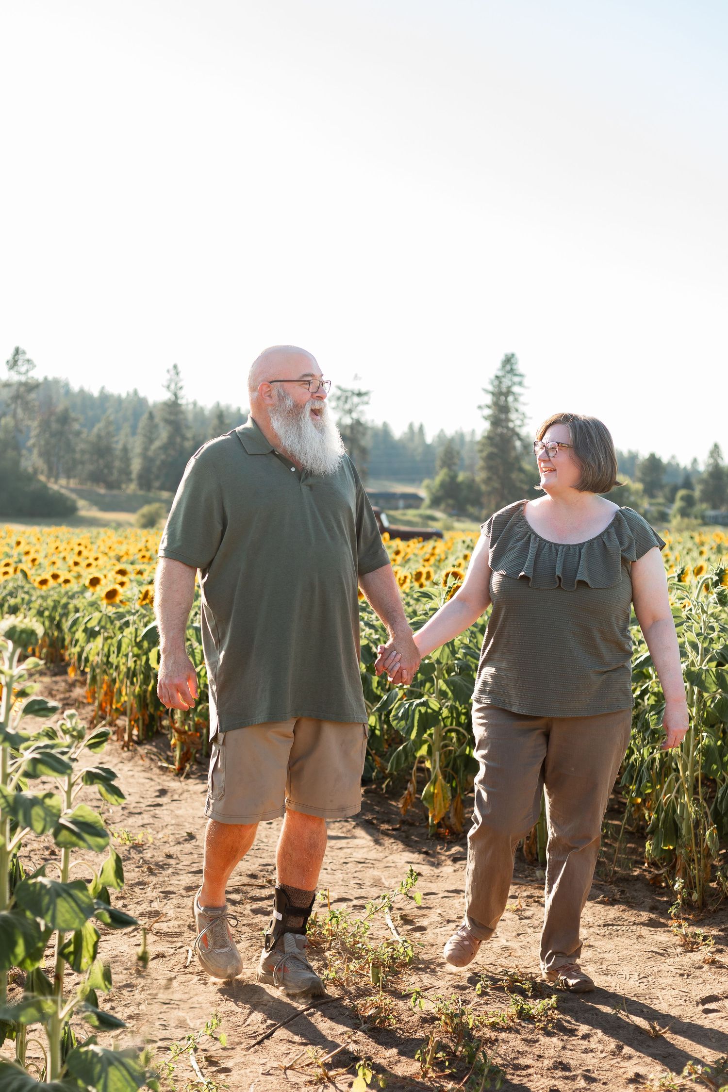 Two people walking hand in hand through a vibrant sunflower field on a sunny day.