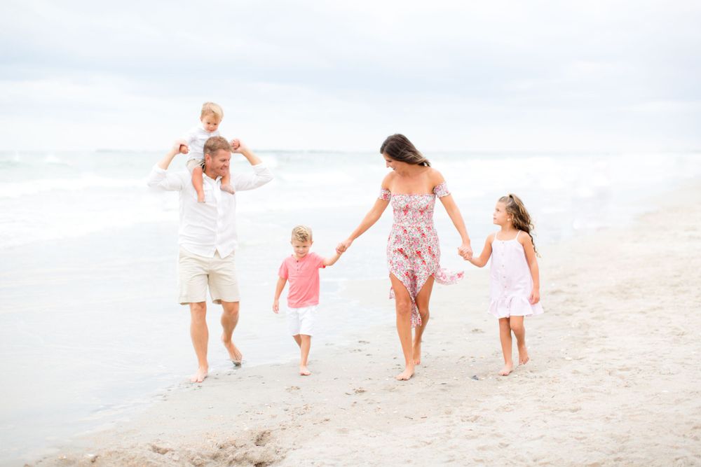 A family walking hand in hand along the beach shore in pastel summer clothing.
