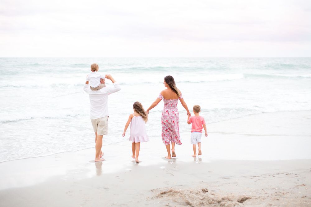A family enjoying a beach walk together while holding hands in summer attire.